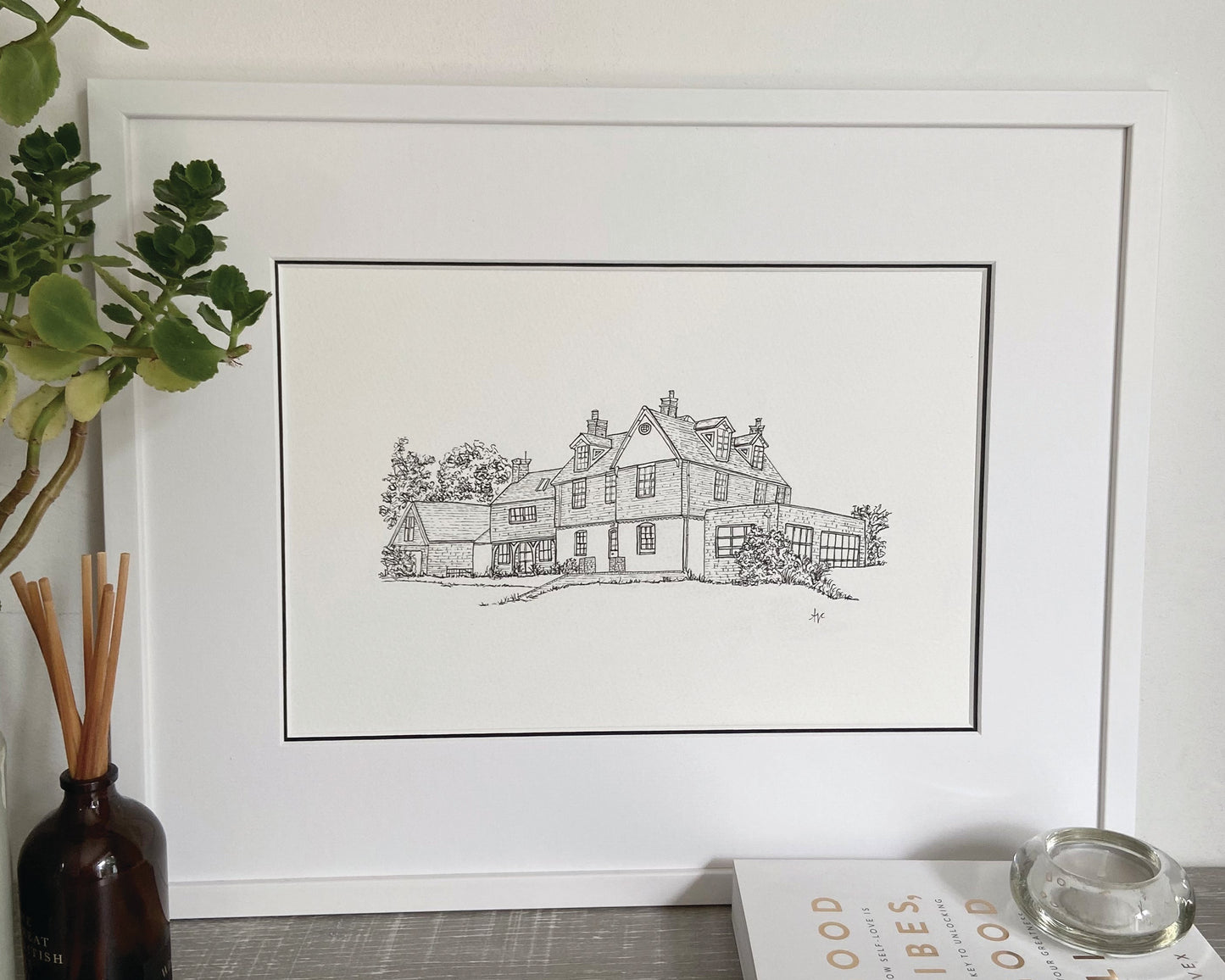 A framed hand-drawn illustration of a house, double mounted with a white frame.
