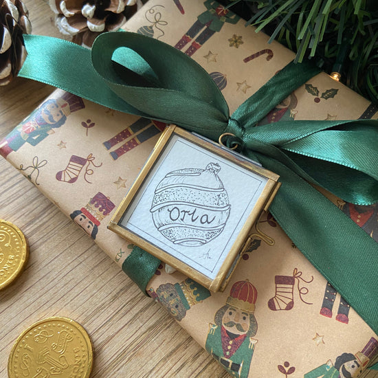 Gift wrapped in festive paper with a green ribbon and a decorative tag featuring 'Ola'.