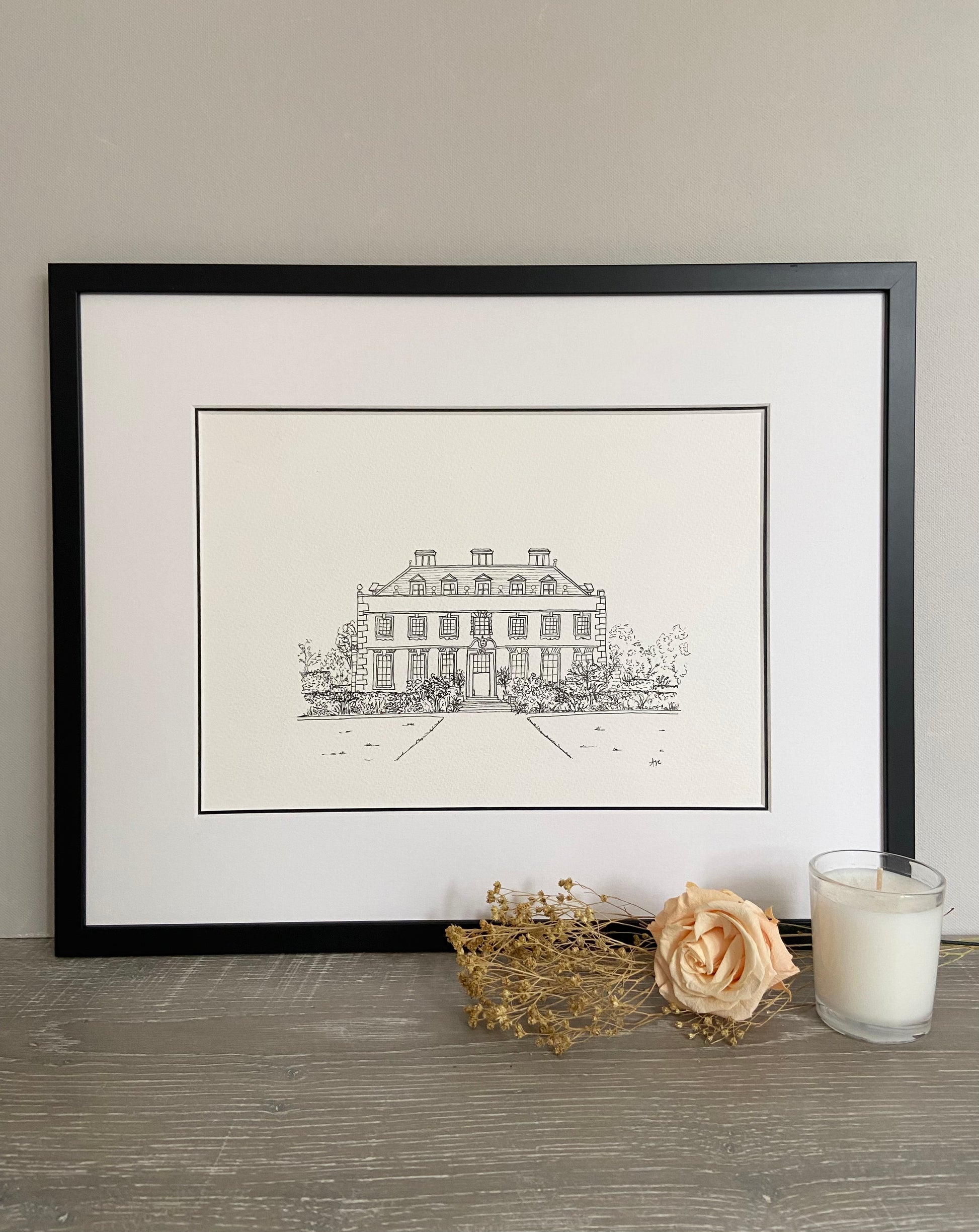 A framed hand-drawn line illustration of a wedding venue. Black line drawing on white paper with a black frame and a double mount