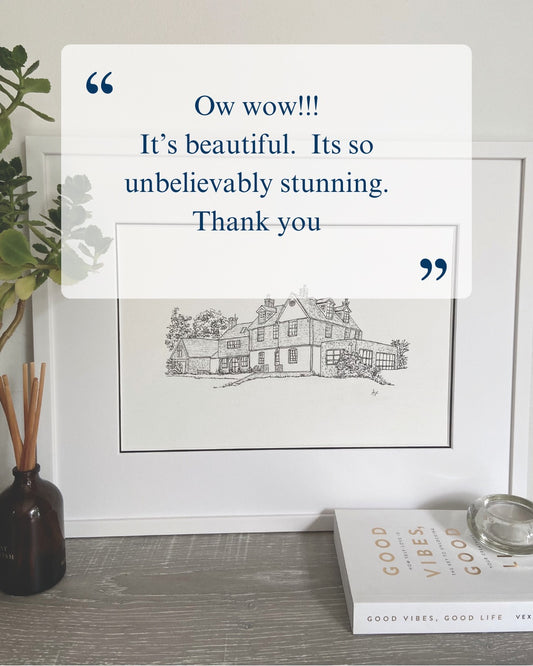 Framed black and white house illustration with decorative elements on a shelf.