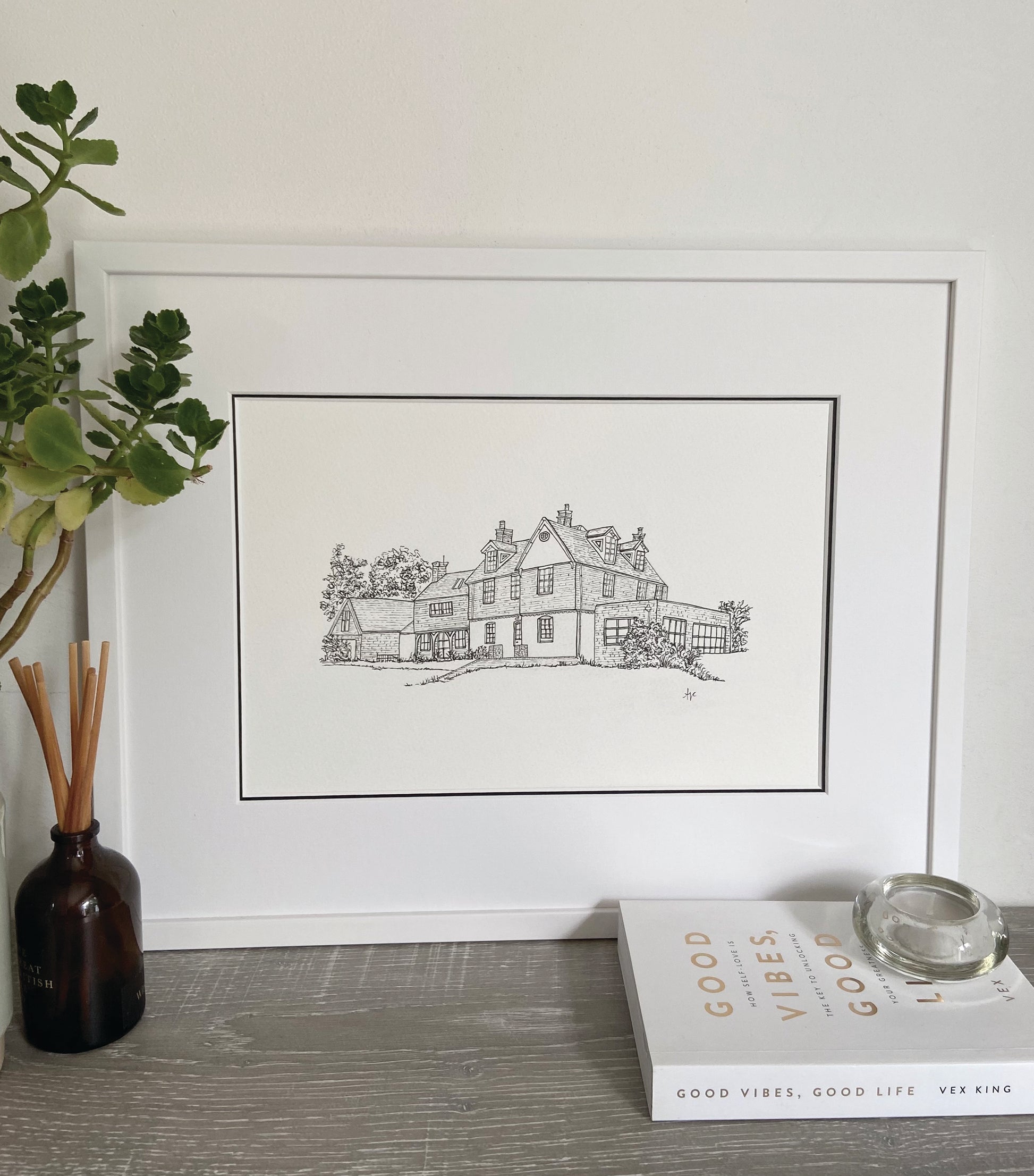 A framed hand-drawn illustration of a house, double mounted with a white frame.