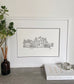 A framed hand-drawn illustration of a house, double mounted with a white frame.