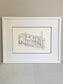 Framed black and white line drawing of a house on a plain wall.