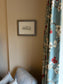Framed picture on a wall next to a floral curtain