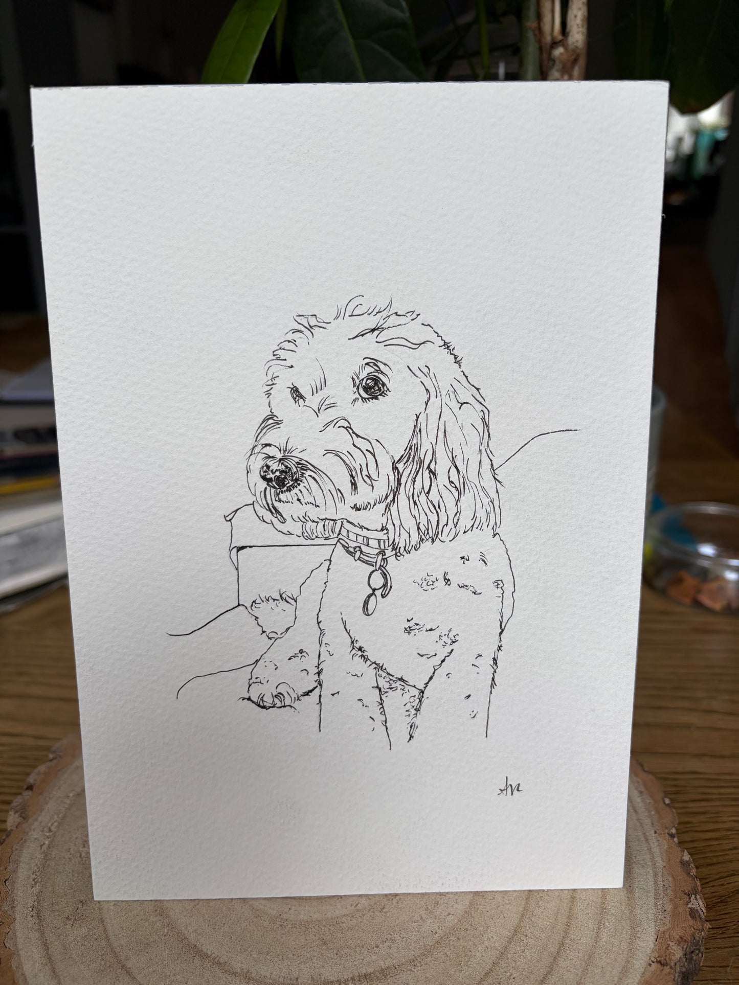 Sketch of a dog on a white card with a wooden surface and plant in the background