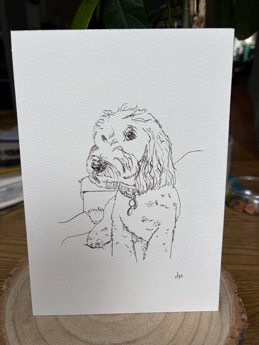 Sketch of a dog on a white card with a wooden surface and plant in the background